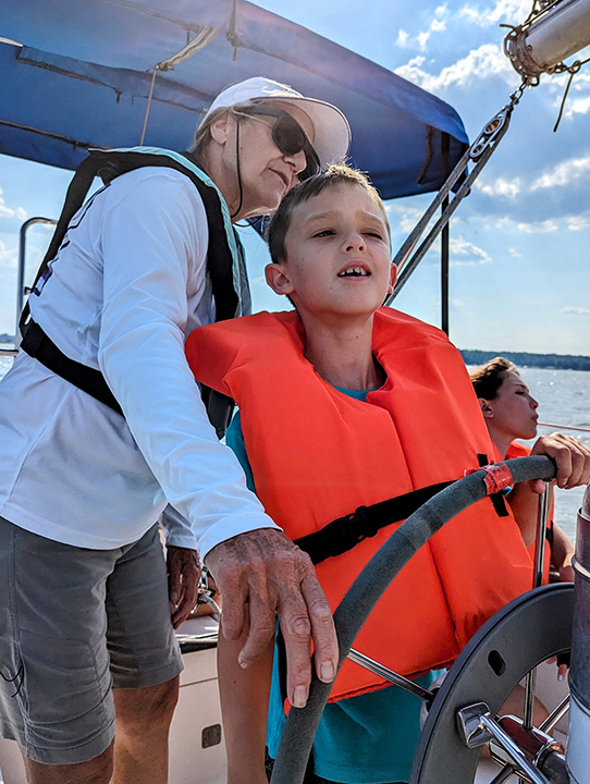 A child at the helm of a boat with a captain providing instruction